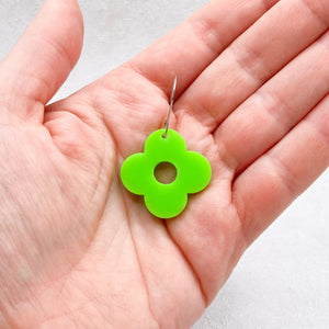 Hand holding green acrylic flower earring with four petals on a light grey background. 