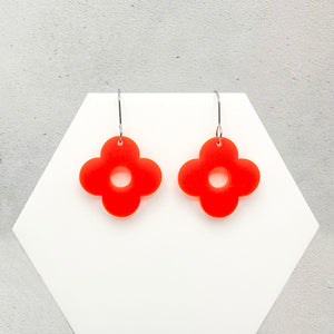 Orange flower-shaped earrings on a white hexagonal stand on a grey background