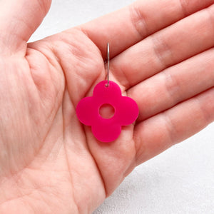 Hand holding a hot pink flower-shaped earring with four petals on a light background.