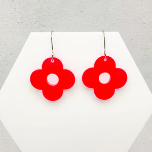 Pink flower-shaped earrings on a white stand with a gray background