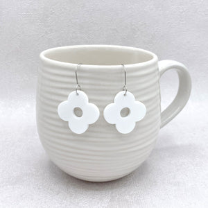 White ceramic mug with white floral earrings hanging inside on a light gray background