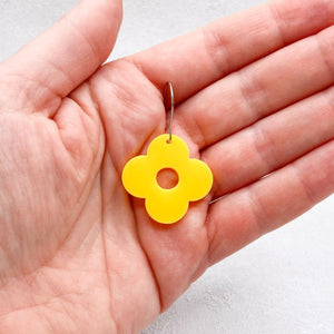 Yellow flower-shaped earring held in a hand against a light background