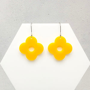 Yellow flower-shaped earrings on a white hexagonal stand on a gray background