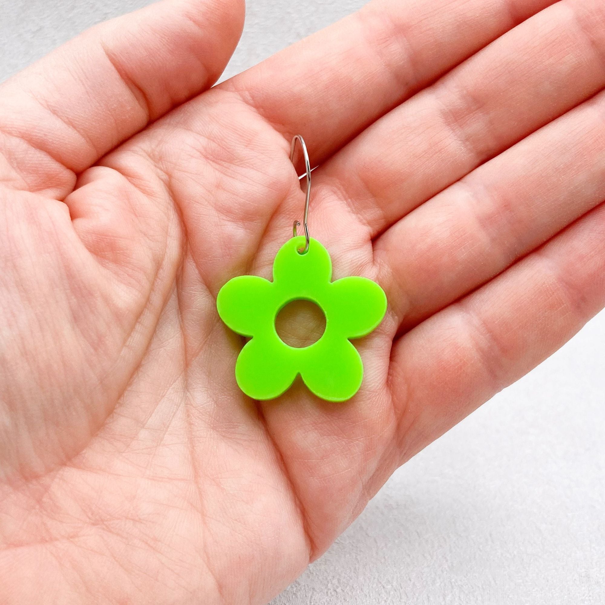 green hippie style flower earring held in a hand on a grey background