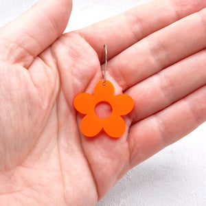 Orange flower-shaped earring held in a hand against a white background