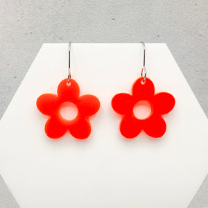Flower-shaped orange earrings on a white hexagonal platform with a gray background