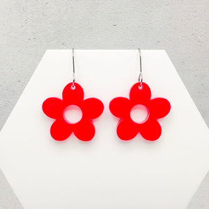 Pink flower-shaped earrings on a white hexagonal stand with a light gray background