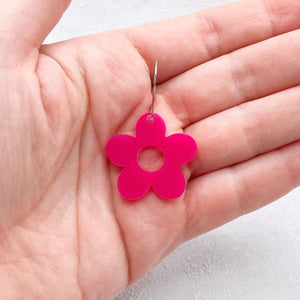 Pink flower-shaped earring held in a hand against a light background