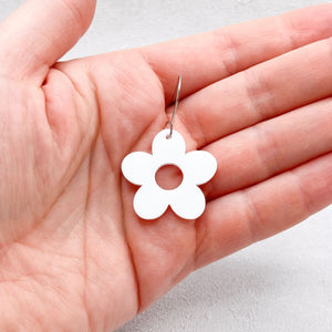 White flower-shaped earring held in a hand against a light background