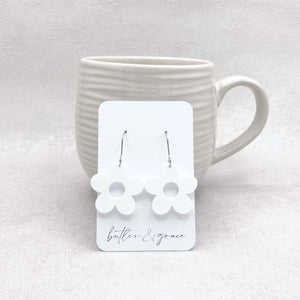 White daisy-shaped earrings on a card with 'butler & grace' branding, displayed against a white mug.