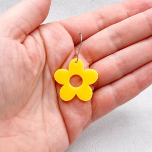 Yellow flower-shaped earring held in a hand against a light background