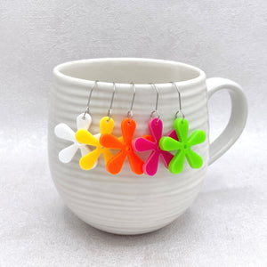 Colorful flower-shaped earrings hanging from a white mug on a light gray background