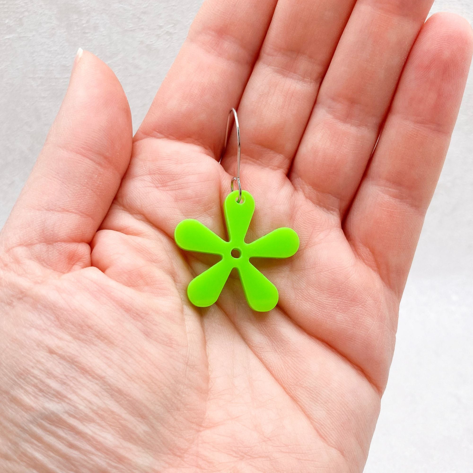 Green flower-shaped earring held in a hand against a neutral background