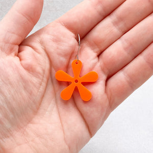 Orange flower-shaped earring held in a hand against a neutral background