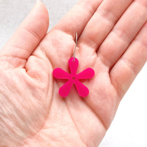 Pink flower-shaped earring held in a hand against a white background
