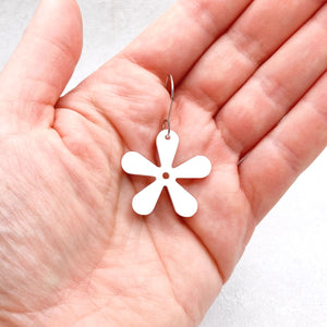White flower-shaped earring held in a hand against a white background