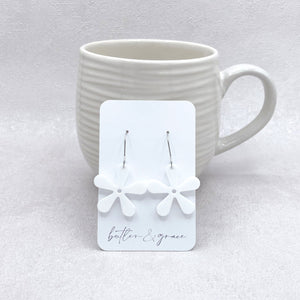 White floral earrings on a card with 'butler & grace' branding, displayed in front of a white mug.
