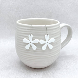 White ceramic mug with white flower-shaped earrings on a light gray background