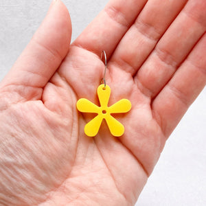 Yellow flower-shaped earring held in a hand against a neutral background