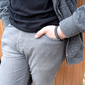 Person wearing grey jeans and a dark shirt and a black wristband with "Addison's Disease", with a wooden background 