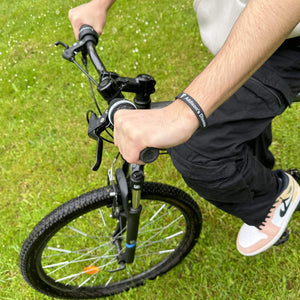 Person riding a bicycle on grass and wearing a black wristband with "Addison's Disease" in white.