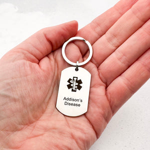 Hand holding a stainless steel keychain with Addison's Disease text on a white background