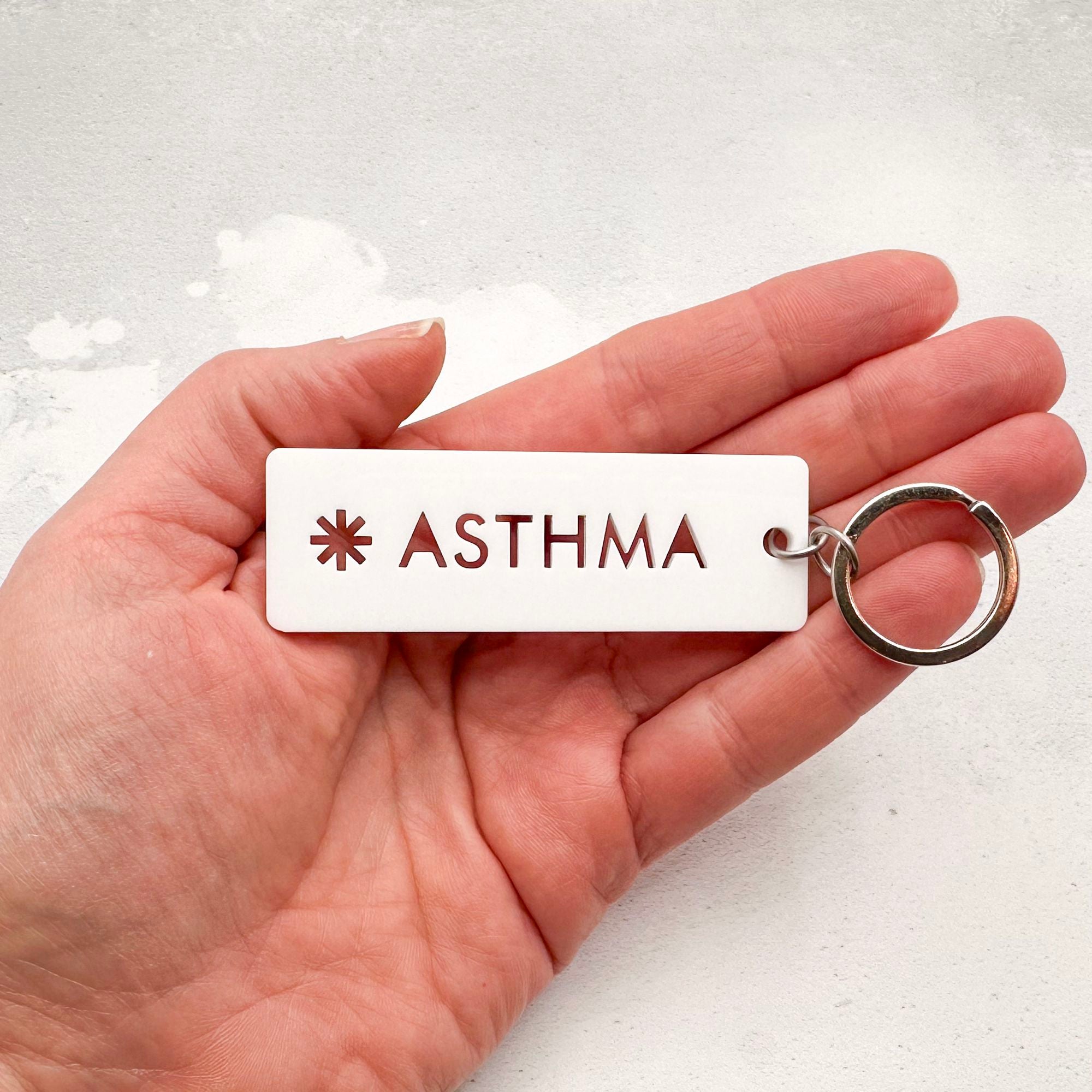 Acrylic asthma medical alert keychain with laser-cut text and silver keyring held in hand