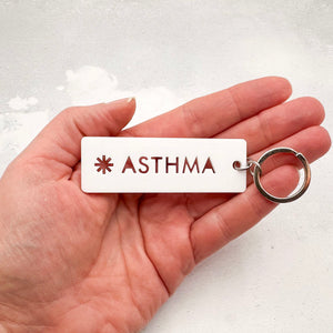 Acrylic asthma medical alert keychain with laser-cut text and silver keyring held in hand