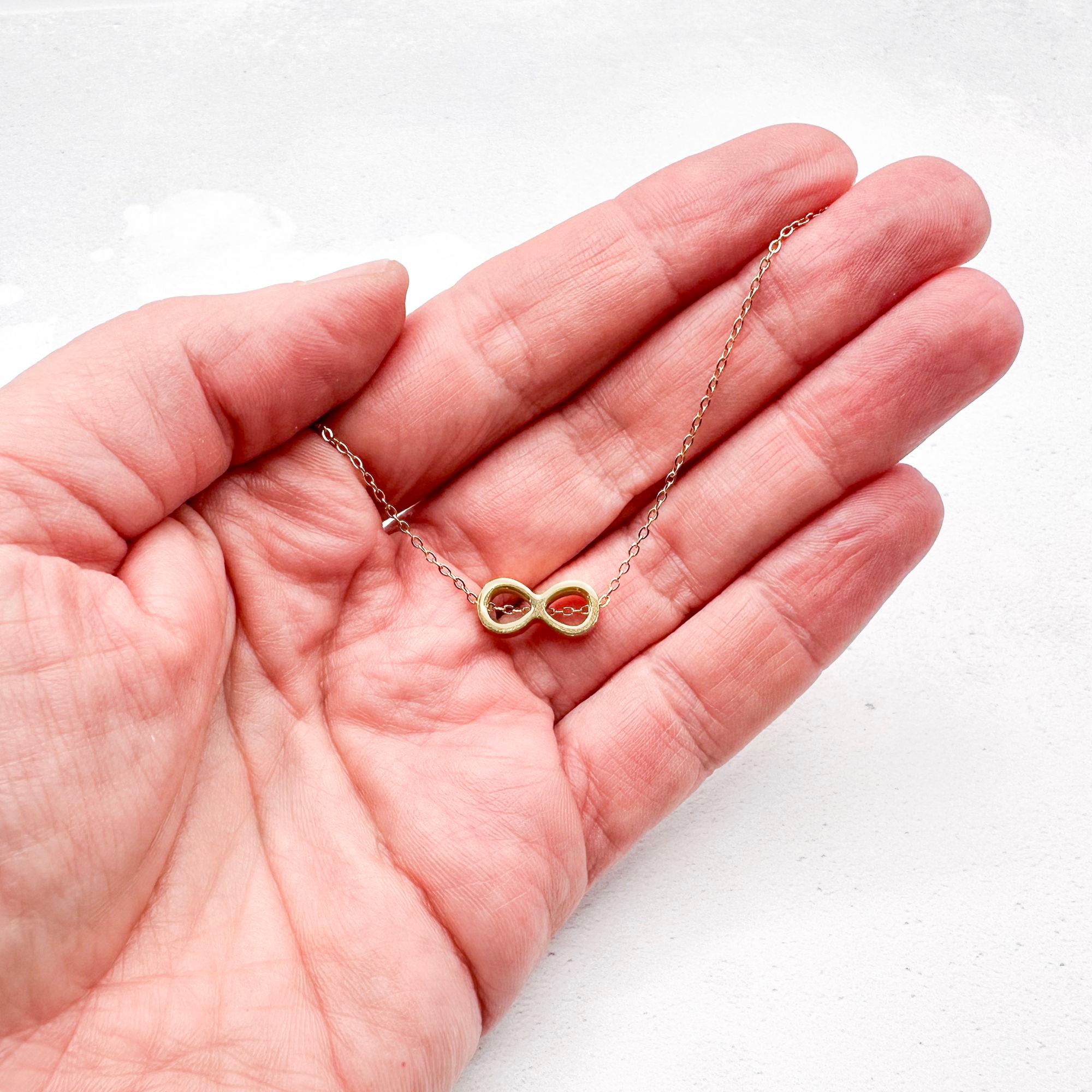 golden-tone stainless steel infinity slider charm on a chain held in hand