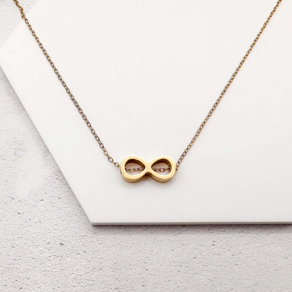 golden-tone stainless steel infinity slider charm on a chain necklace against a white background
