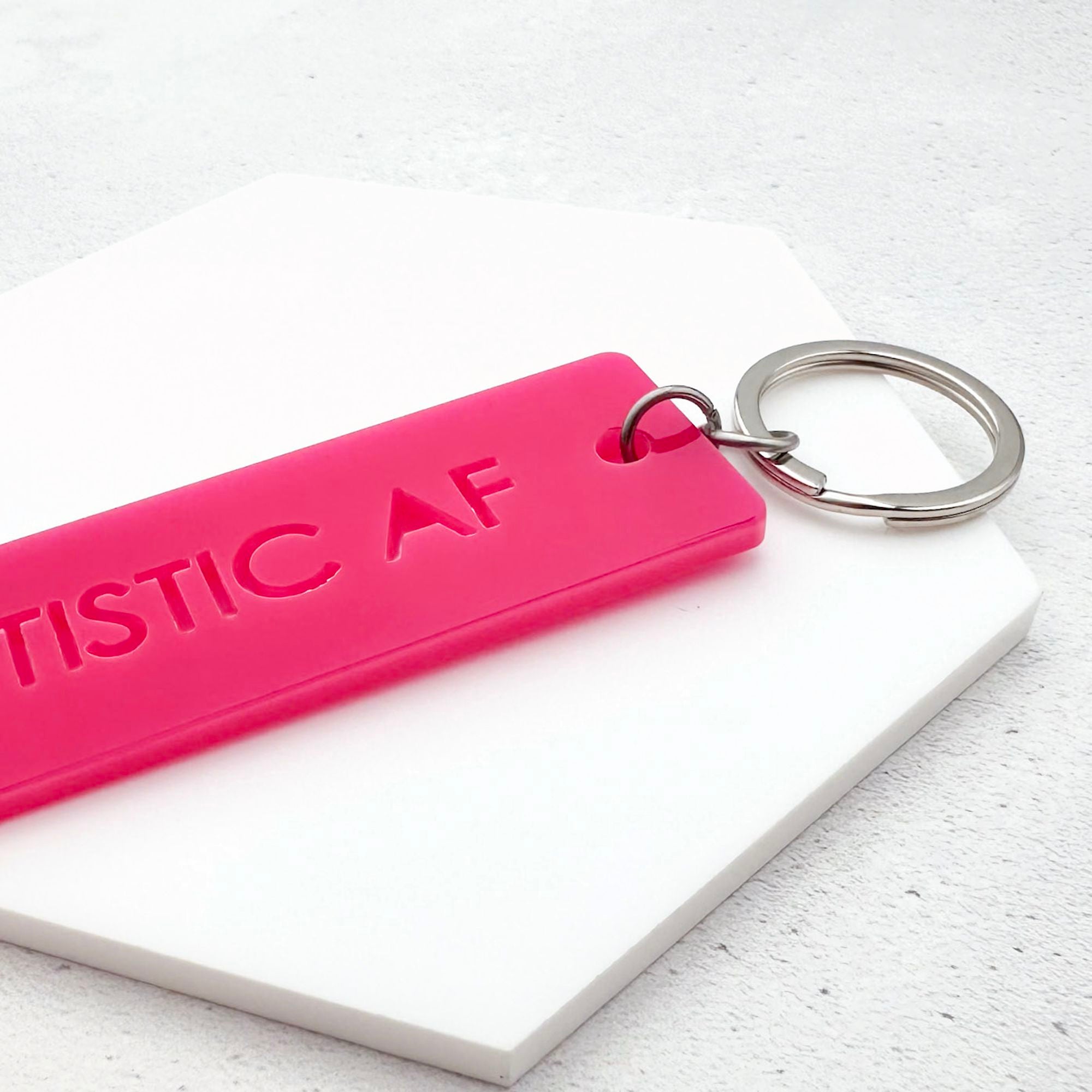 Pink keychain with 'AUTISTIC AF' text on a white surface