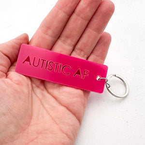 hot pink acrylic keychain with 'Autistic AF' text held in hand