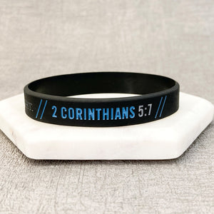 Black wristband with '2 Corinthians 5:7' text on a white surface