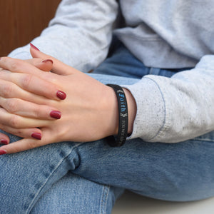 Person wearing a black bracelet with visible text, sitting on a couch.