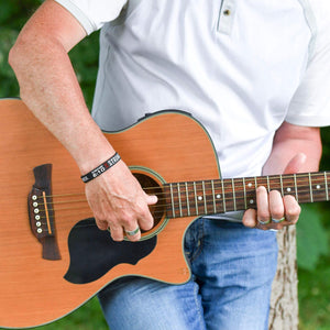 Person holding an acoustic guitar with a blurred natural background and wearing a black band