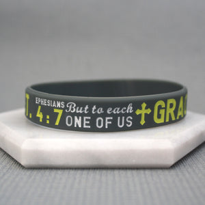 Gray wristband with yellow text and cross symbol on a gray background