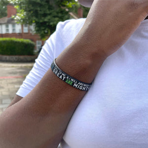 Person wearing a black bracelet with text on an arm, outdoors.