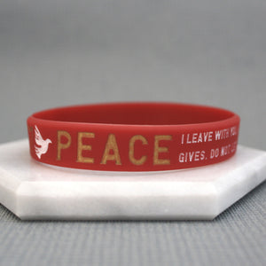 Red wristband with gold text and a dove symbol on a gray background