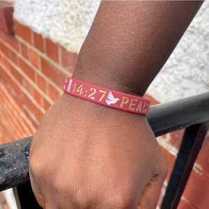 Red wristband on a wrist with gold text and a white dove