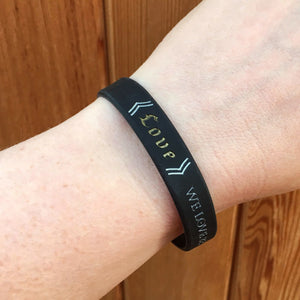 Black wristband with text on a wrist against a wooden background