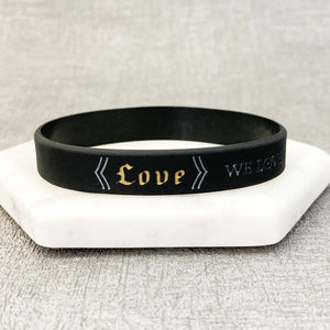 Black wristband with 'Love' text on a white stand against a gray background