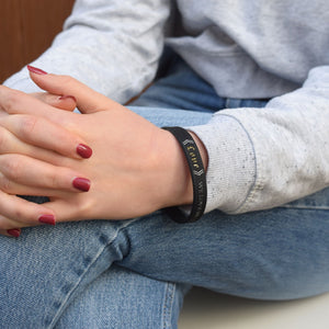 Person wearing a black bracelet with bible verse text, sitting on a couch.