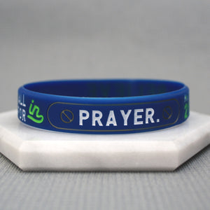 Blue wristband with 'PRAYER' printed on it, placed on a white surface.