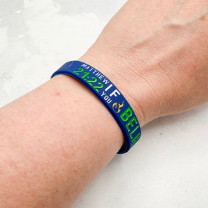 Blue and green wristband with text on a person's wrist against a white background