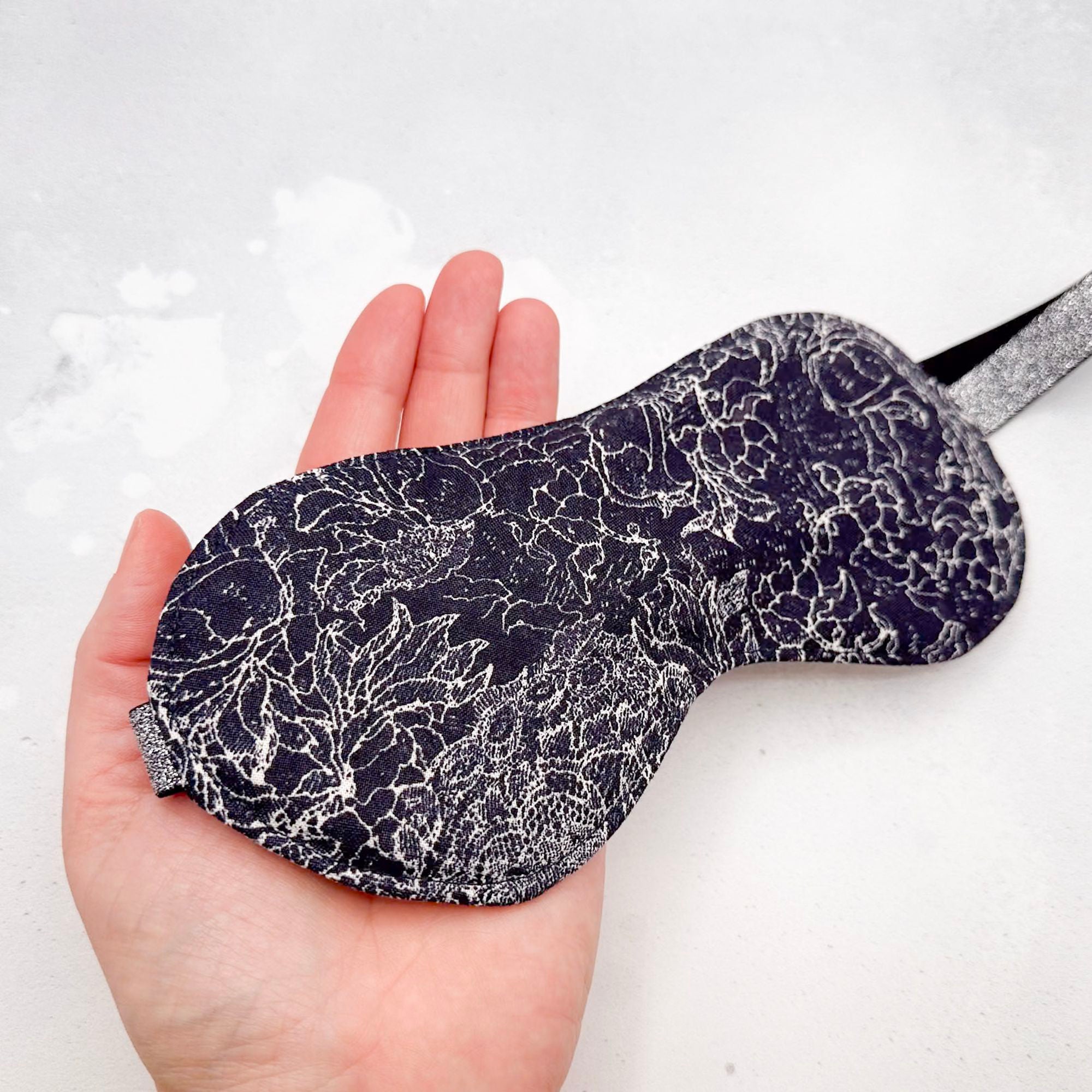 Sleep mask with black pattern held in a hand 