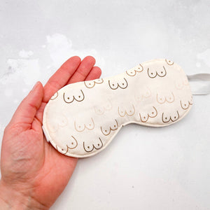 Hand holding a cream-coloured eye mask with breasts pattern 