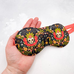 Sleep mask with skull and floral pattern held in a hand 