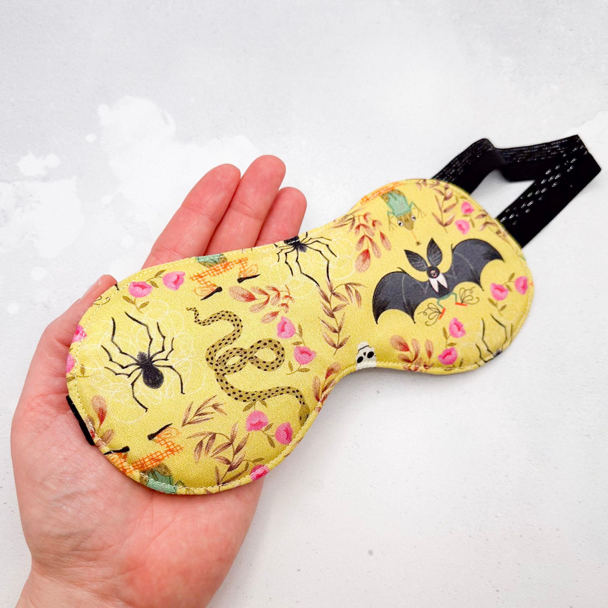 Hand holding a yellow sleep mask with Halloween-themed design