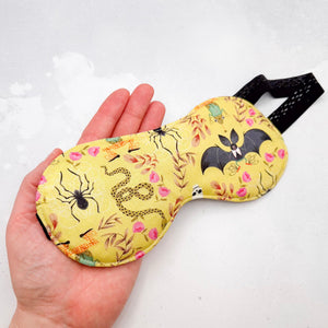 Hand holding a yellow sleep mask with Halloween-themed design