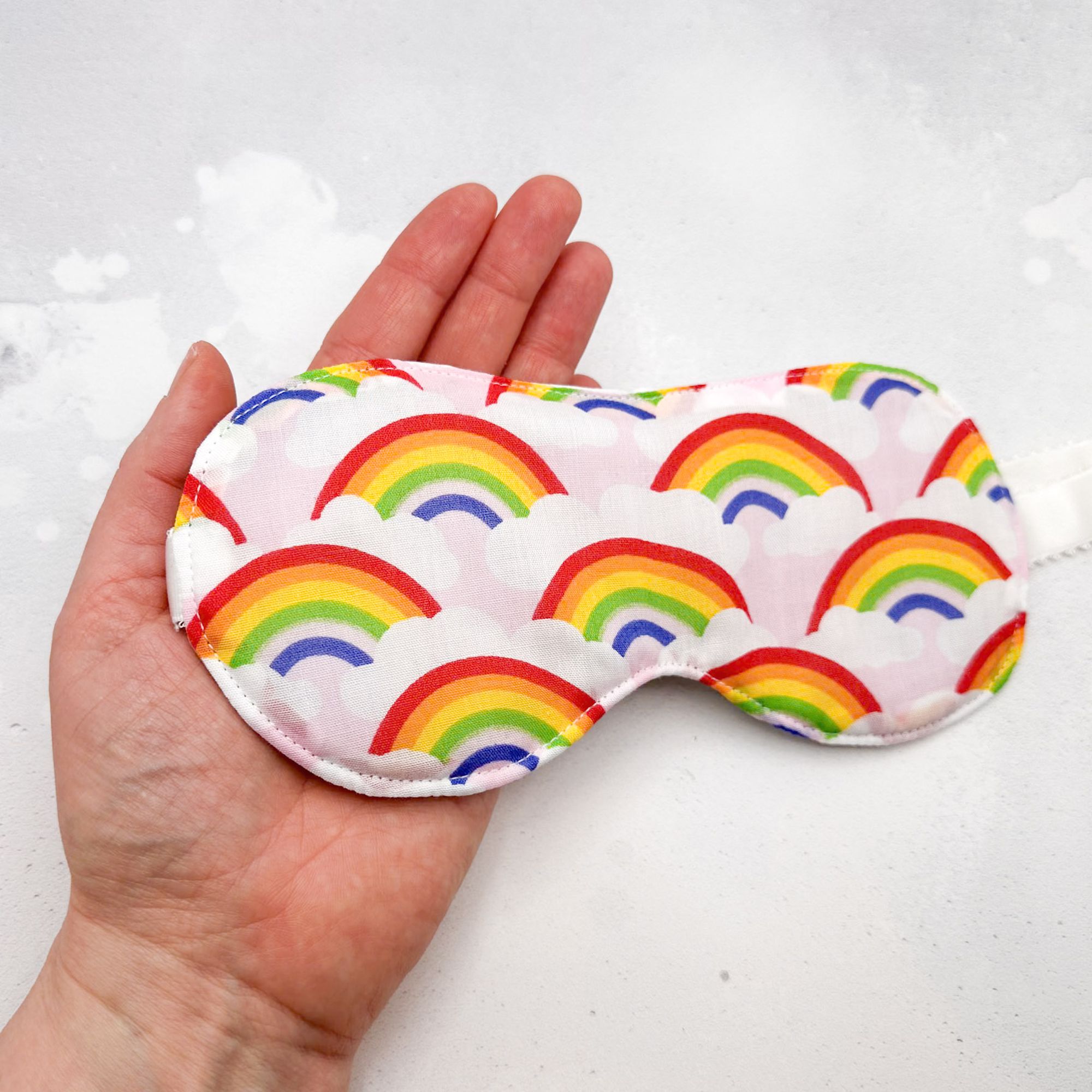 Hand holding a sleep mask with rainbow pattern 